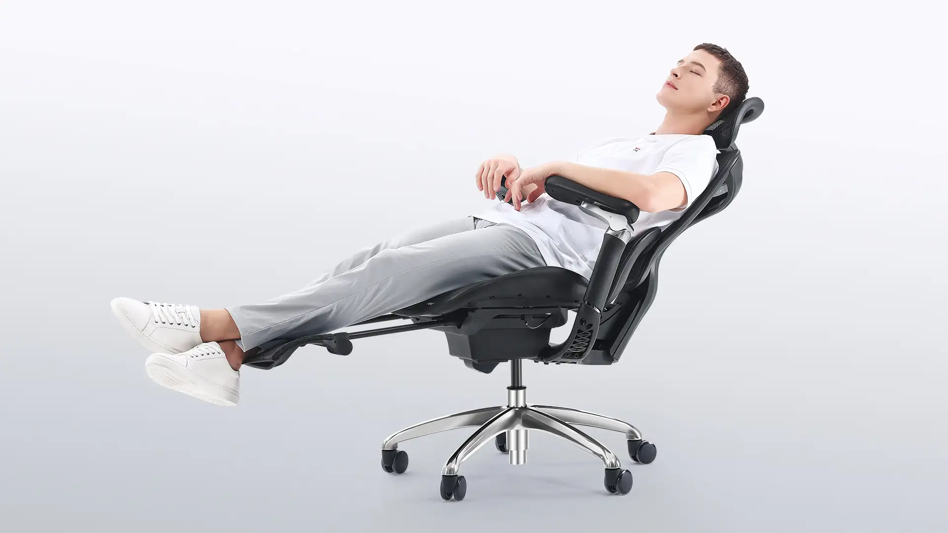 A man fully reclining in an ergonomic office chair with a footrest, dressed in casual wear, demonstrating the chair's comfort for relaxation.